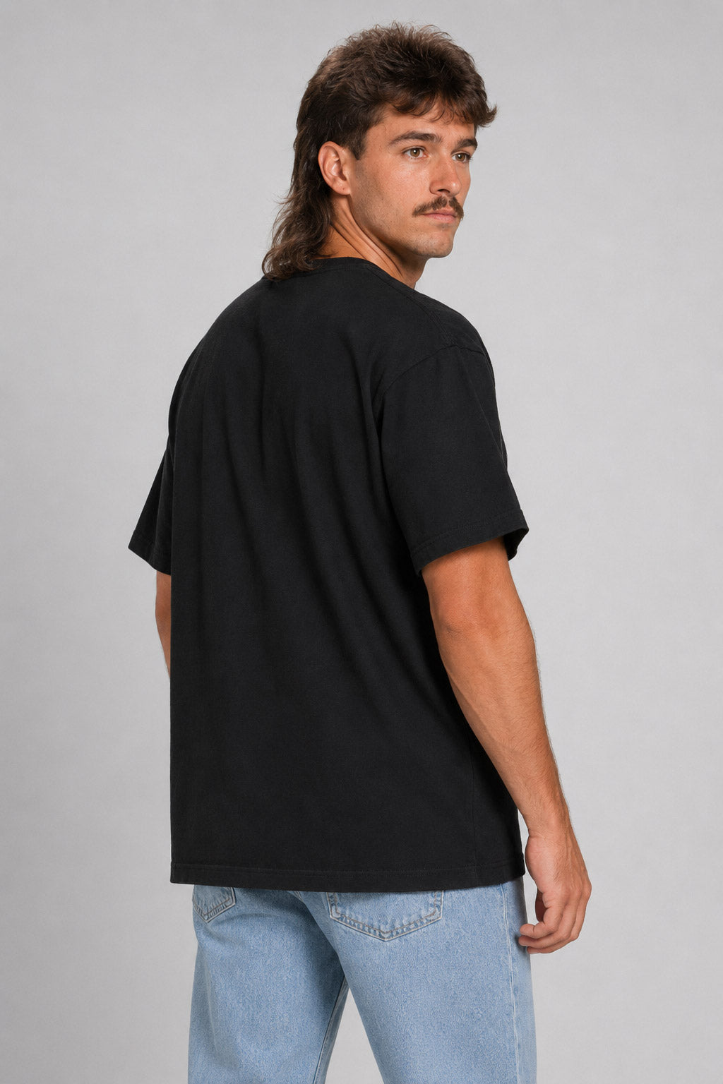 A man with a mullet hairstyle and mustache wearing a black short-sleeve t-shirt and light blue jeans, photographed from the back against a light gray studio background. #black