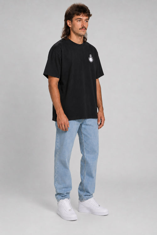 A man modeling a black short-sleeve t-shirt with a small white graphic on the left chest, paired with light blue jeans and white sneakers, against a neutral gray studio background. #black