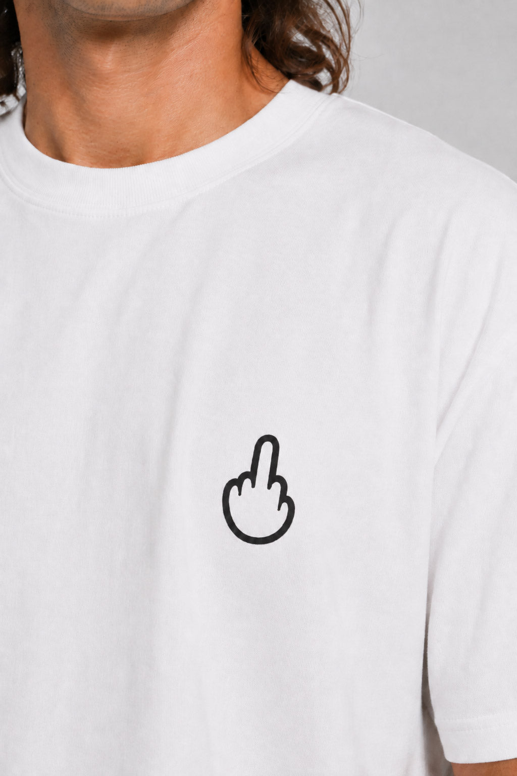 A close-up of a person wearing a white crew-neck t-shirt with a small black outline graphic of a middle finger on the left chest. #white